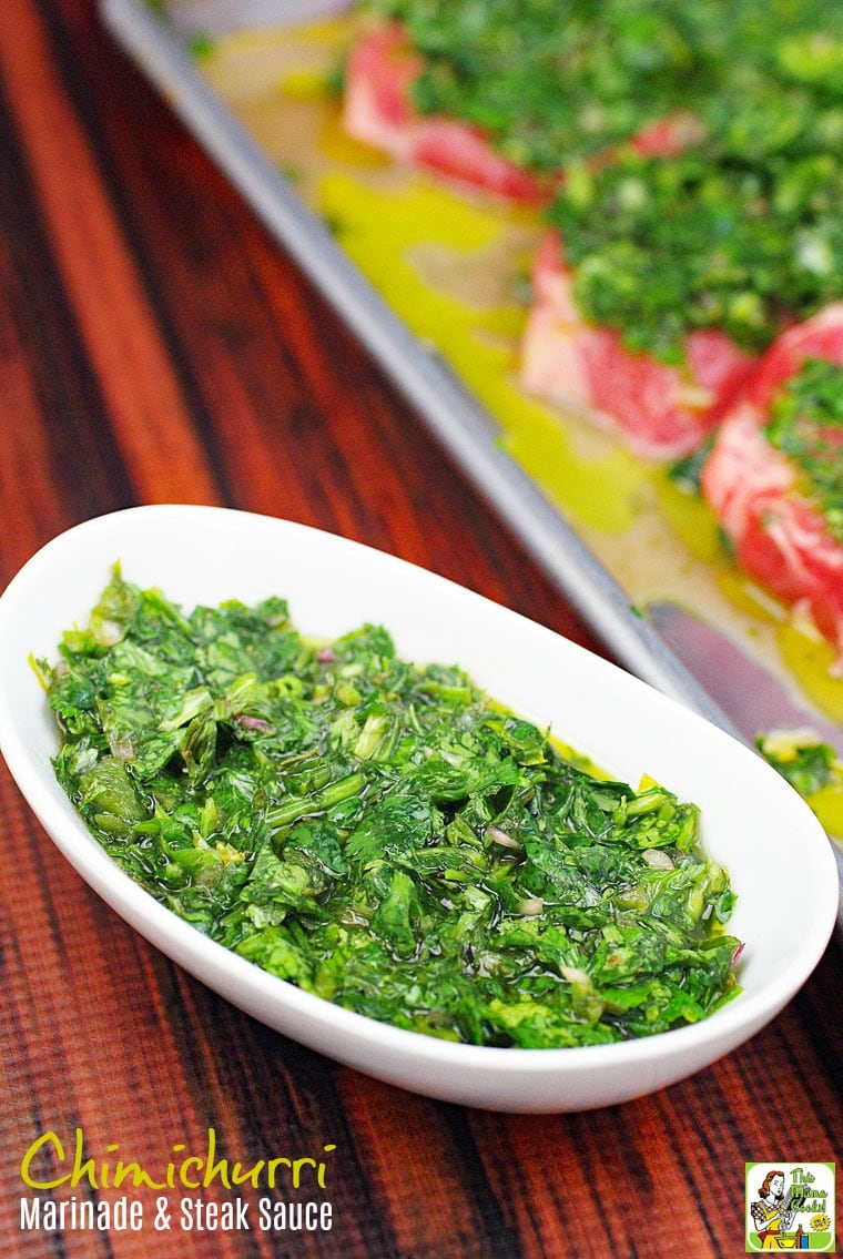 A white bowl of chimichurri marinade and sauce and a tray of chimichurri steak in the background.