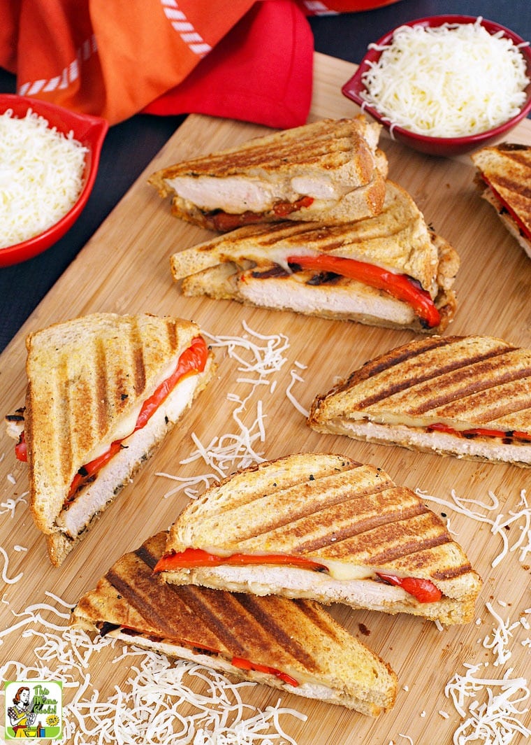 Chicken paninis on a wooden cutting board with bowls of shredded cheese.