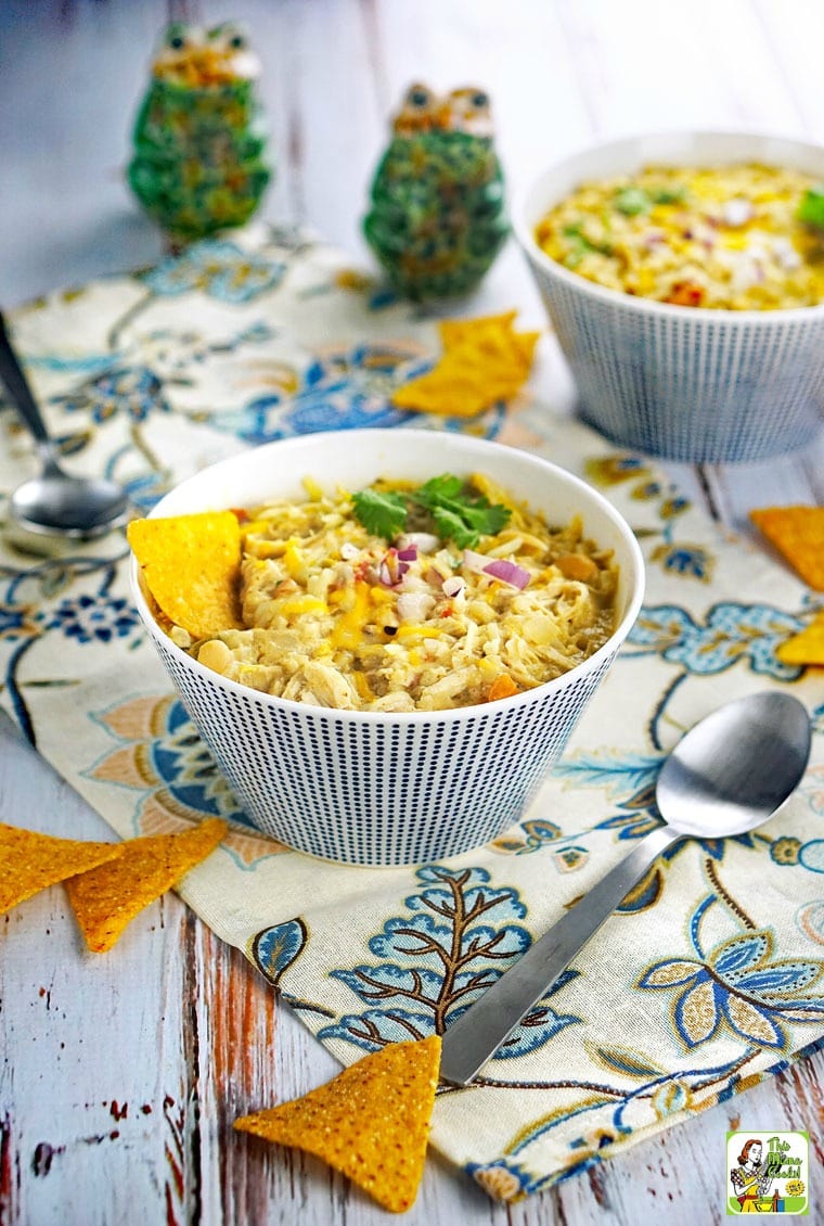 A bowl of Slow Cooker Creamy Verde Chicken Chili with chips and spoons.