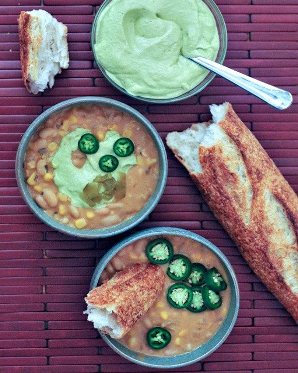 Overhead view of bowls of Smoky White Chili with Hatch Avocado Cream with French bread.