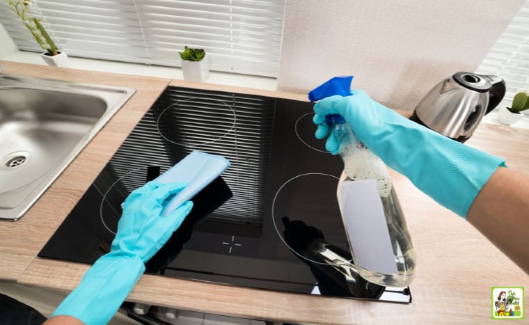 Person's hands in blue gloves cleaning induction cooktop stove in a sunny modern kitchen.