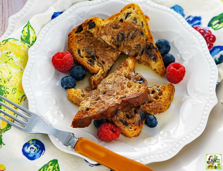 Gluten Free French Toast on a white plate with berries and a fork with a floral napkin.