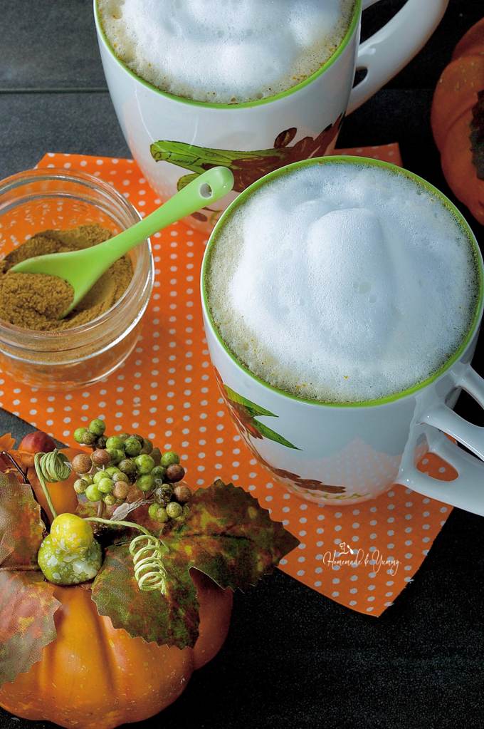 A mug of Real Pumpkin Latte with a jar of spices on a orange and white polka dot placemat.