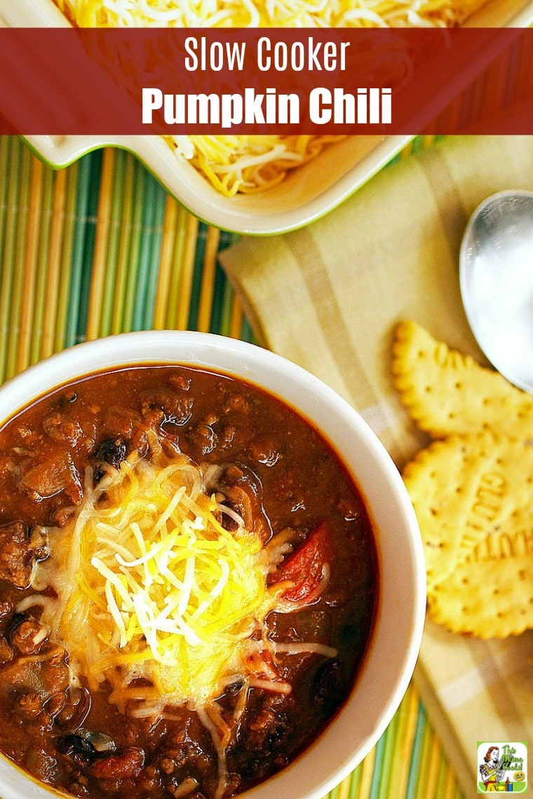 A bowl of Slow Cooker Pumpkin Chili with crackers, napkin, and a spoon on a colorful bamboo mat.