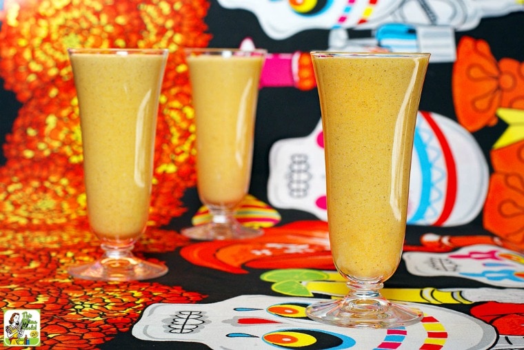 Three tall glasses of pumpkin smoothie shakes on Day of the Dead tablecloth.