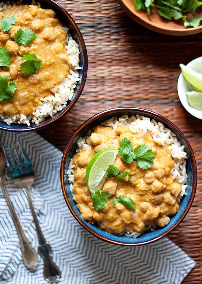 Bowls of Slow Cooker Pumpkin, Chickpea, & Red Lentil Curry served on rice with lime with forks, napkins, and slices of lime.
