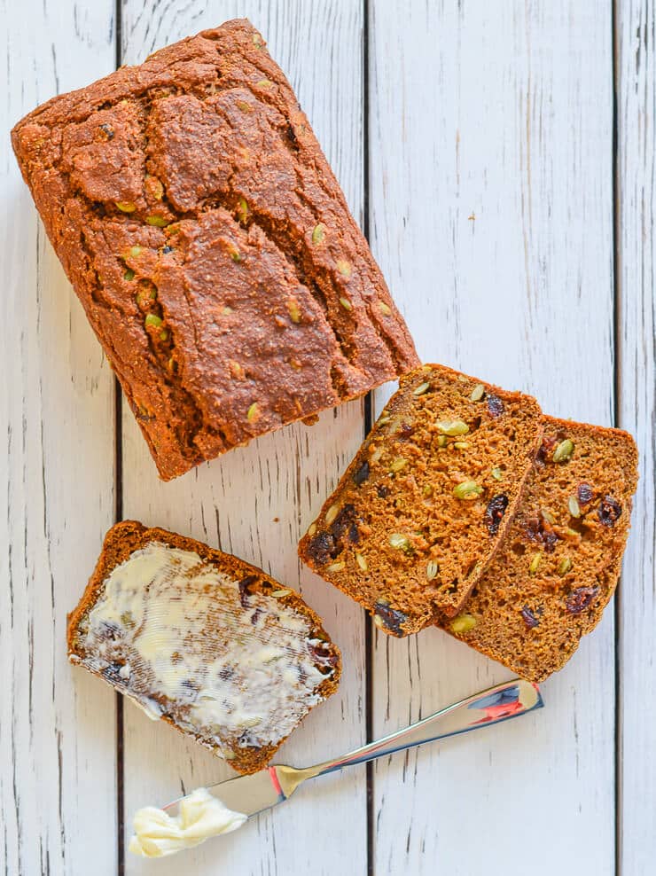 Slices of Vegan Pumpkin Bread with Cranberries & Pumpkin Seeds with knife and butter.