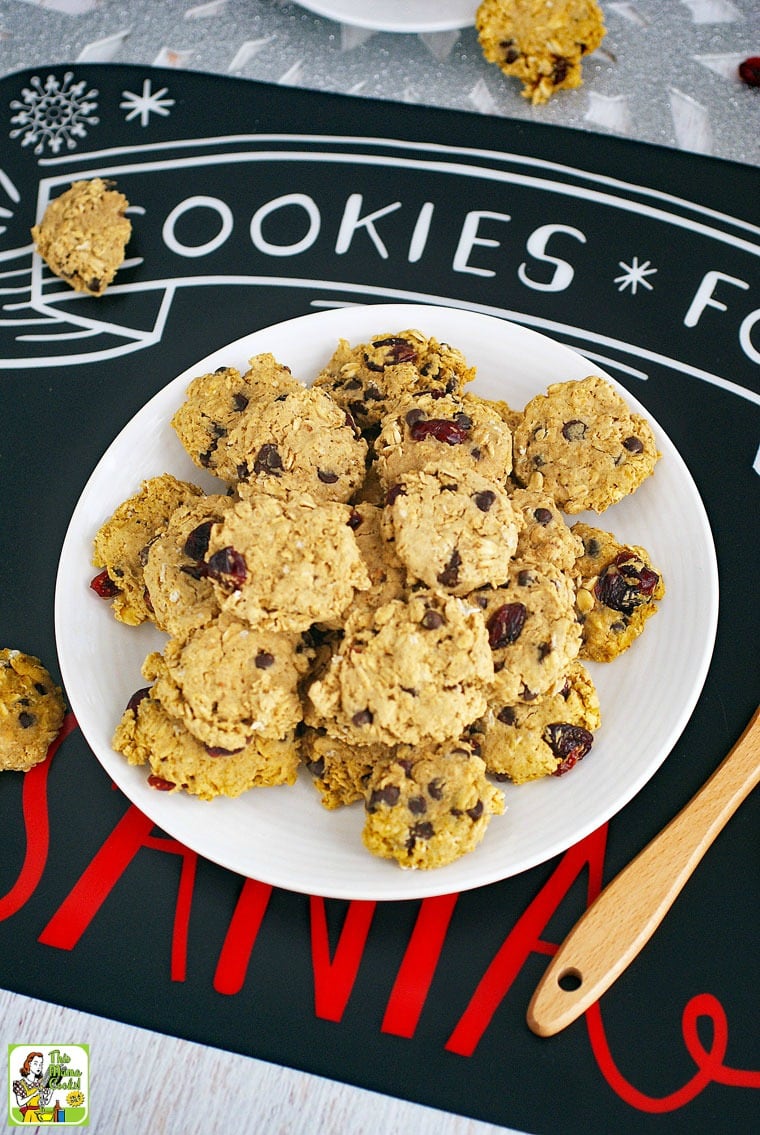 Cookies for Santa placemat with a plate of gluten free oatmeal cookies with chocolate chips and raisins, a glass of milk with a straw, and a Santa spatula.