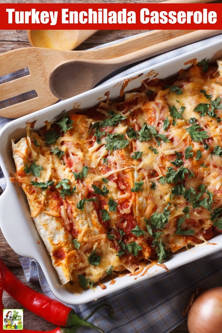 Cheesy turkey enchiladas in a casserole baking dish placed on a blue and white napkin, with red peppers and onions, next to wooden serving spoons.