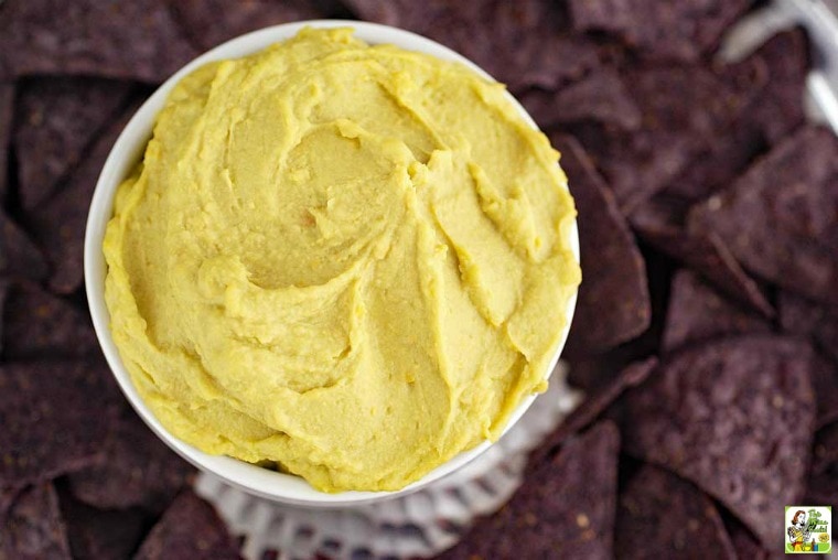 Overhead shot of a bowl of avocado hummus with blue tortilla chips.