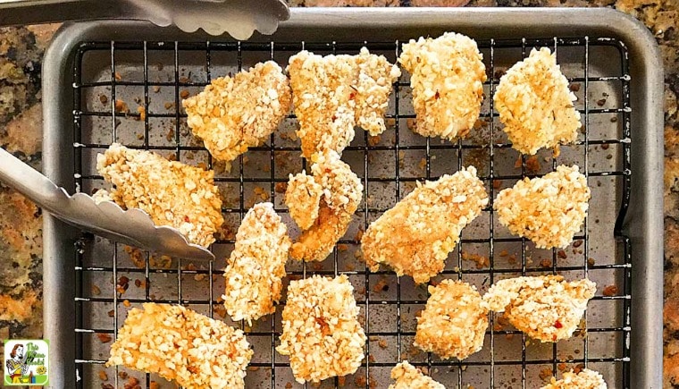 Homemade Chicken Nuggets on a wire rack over a baking sheet with tongs.