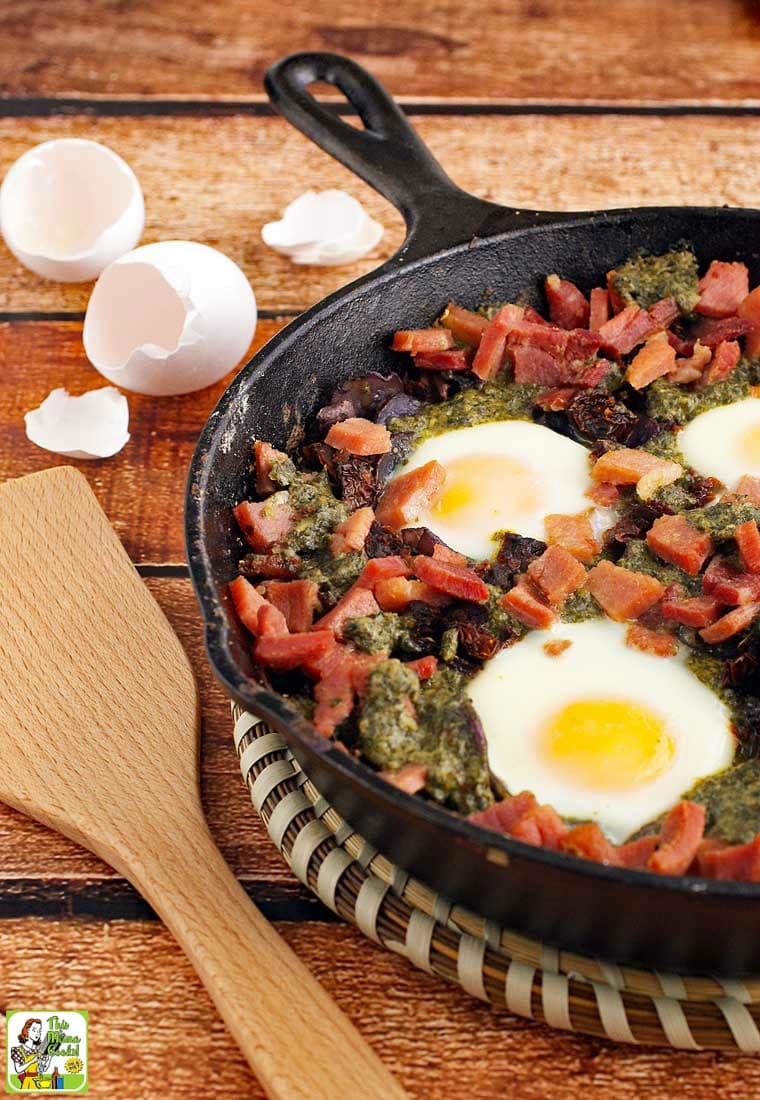 Baked eggs, ham, potatoes, and pesto in a skillet with a wooden spatula.