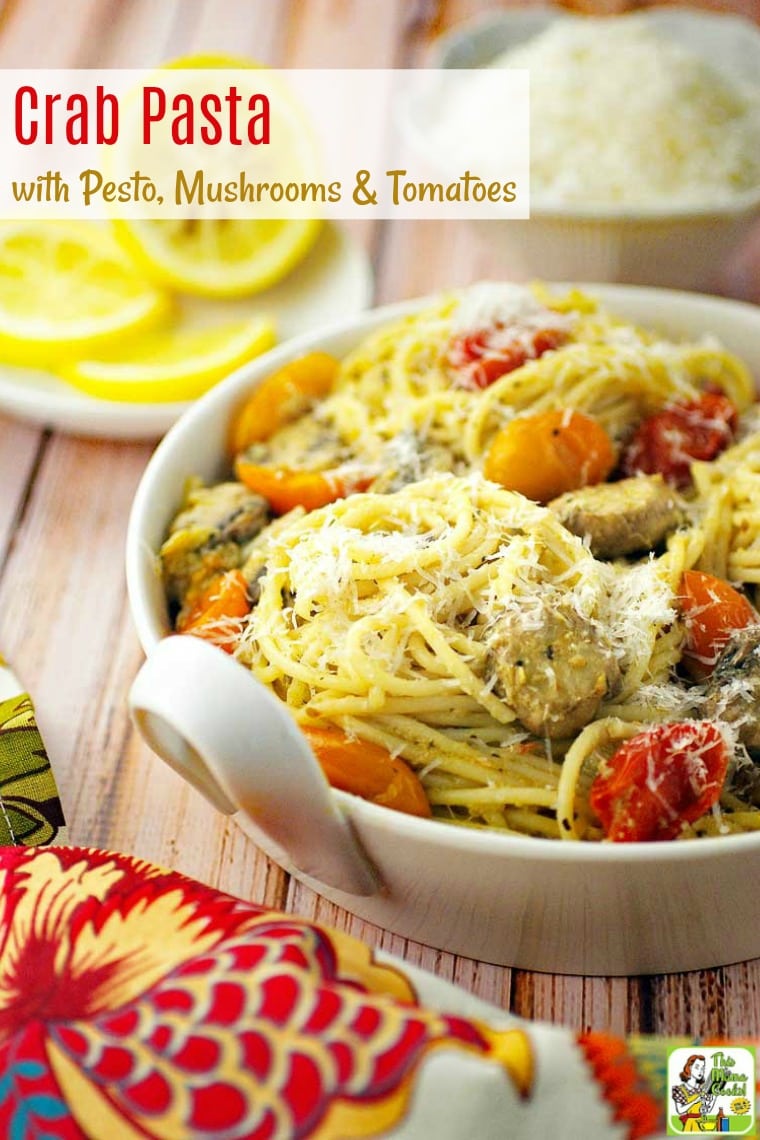 A bowl of Pasta with crab, pesto, mushrooms and tomatoes with a colorful napkin and plate of sliced lemons in the background.