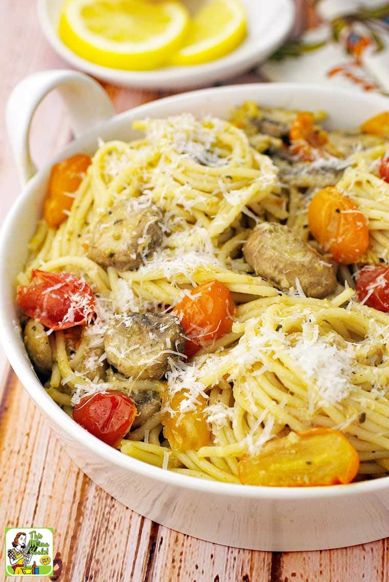 A bowl of spaghetti with crab, pesto, mushrooms, tomatoes and grated cheese.