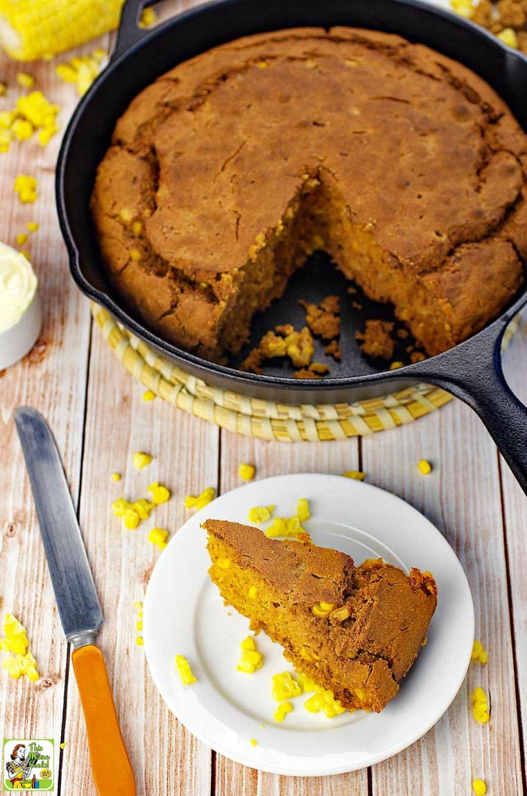 Overhead shot of skillet cornbread, a slice of cornbread on a white plate, a knife, and kernels of corn.