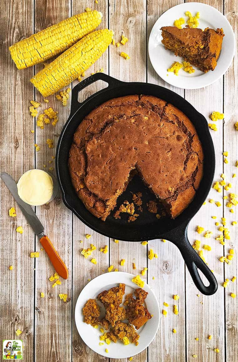 Overhead shot of skillet cornbread, white plates of cornbread, a knife, a small bowl of butter, and corncobs on a tabletop.