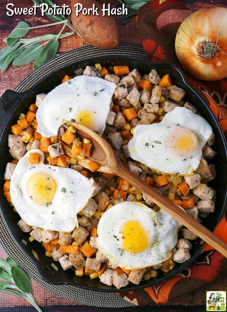 A cast iron skillet of Sweet Potato Pork Hash, sunny side up eggs, and a wooden spoon, surrounded by ingredients - onion, sweet potato and sage