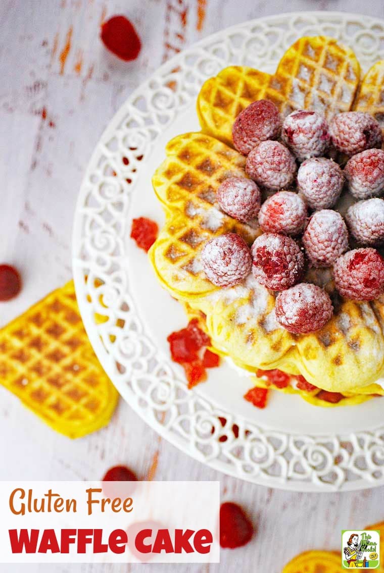 Overhead view of a waffle cake with cream cheese, jam, and sugared raspberries on a white cake stand.