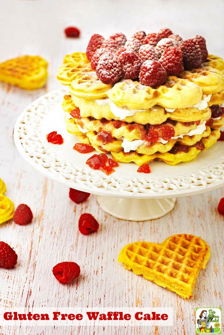 Gluten Free Waffle Cake with raspberries and powdered sugar on a white cake stand.