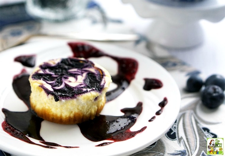 Mini cheesecake with blueberry swirl on a white plate with fresh blueberries.
