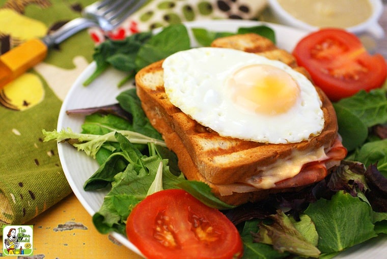 A plate with lettuce, a grilled ham and cheese Croque Monsieur sandwich with an egg, and sliced tomatoes