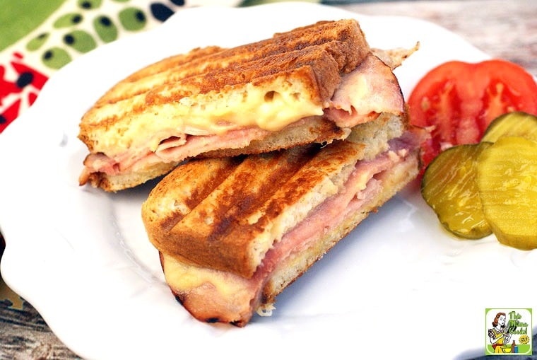 Grilled ham and cheese sandwich with pickles and sliced tomatoes.