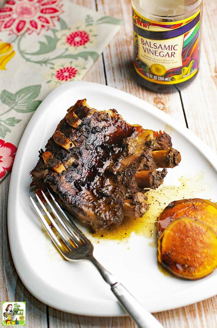 Crock-Pot Ribs and sweet potato with fork on white plate with bottle of balsamic vinegar.