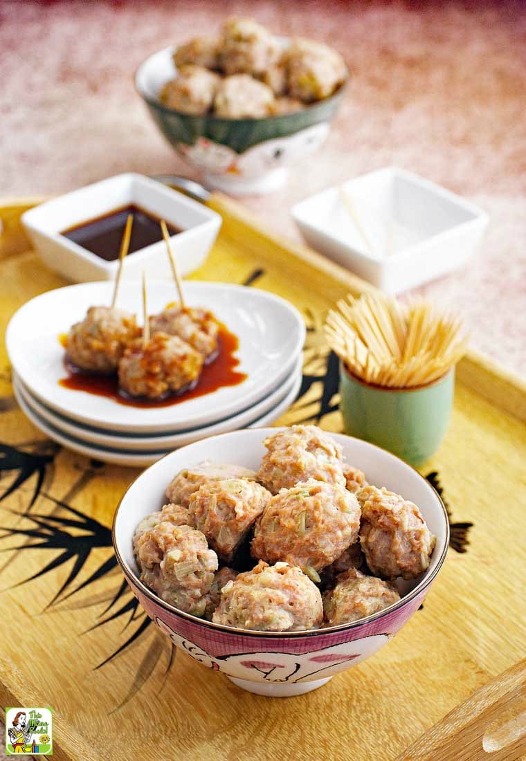 A tray of Asian style pork meatball appetizers with a bowl of dipping sauce.