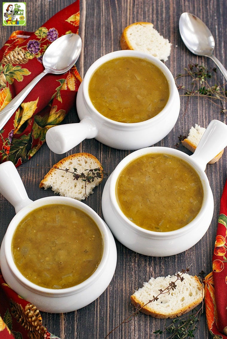 Bowls of split pea soup with soup spoons, pieces of bread, sprigs of thyme, red napkins, on a wooden tabletop.