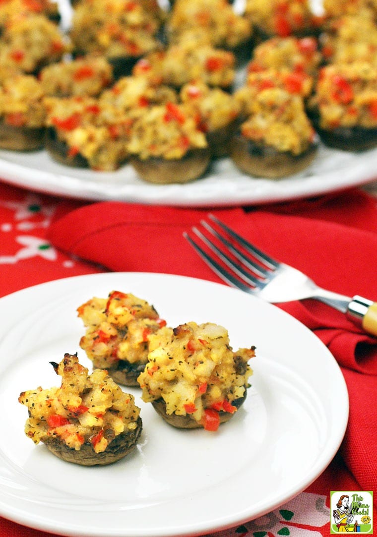 A plate and platter of crab stuffed mushrooms with fork and red napkins.