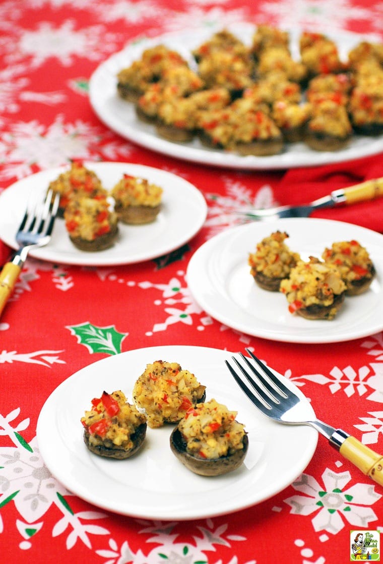 Plates and a platter of stuffed mushrooms with forks on a holiday tablecloth.