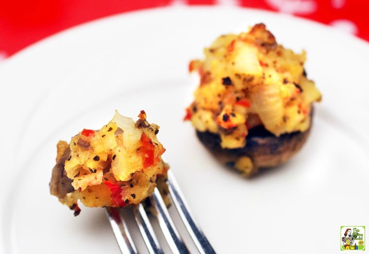 Closeup of stuffed mushroom appetizers speared on a fork on a white plate.