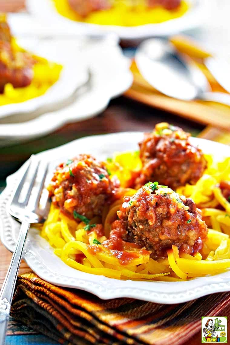 Closeup of a plate of porcupine meatballs served on butternut squash zoodles with a fork and napkin.