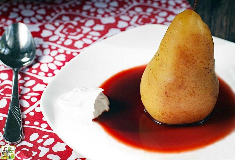 A dish with a Slow Cooker Poached Pear in cherry sauce on a red and white napkin with spoon.