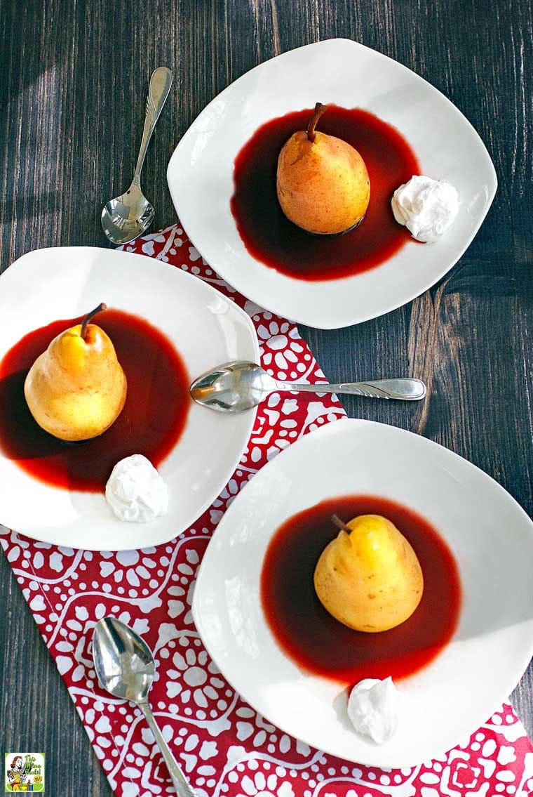 Slow Cooker Poached Pears in cherry sauce with a dollop of coconut whipped cream on white plates with spoons and napkins.