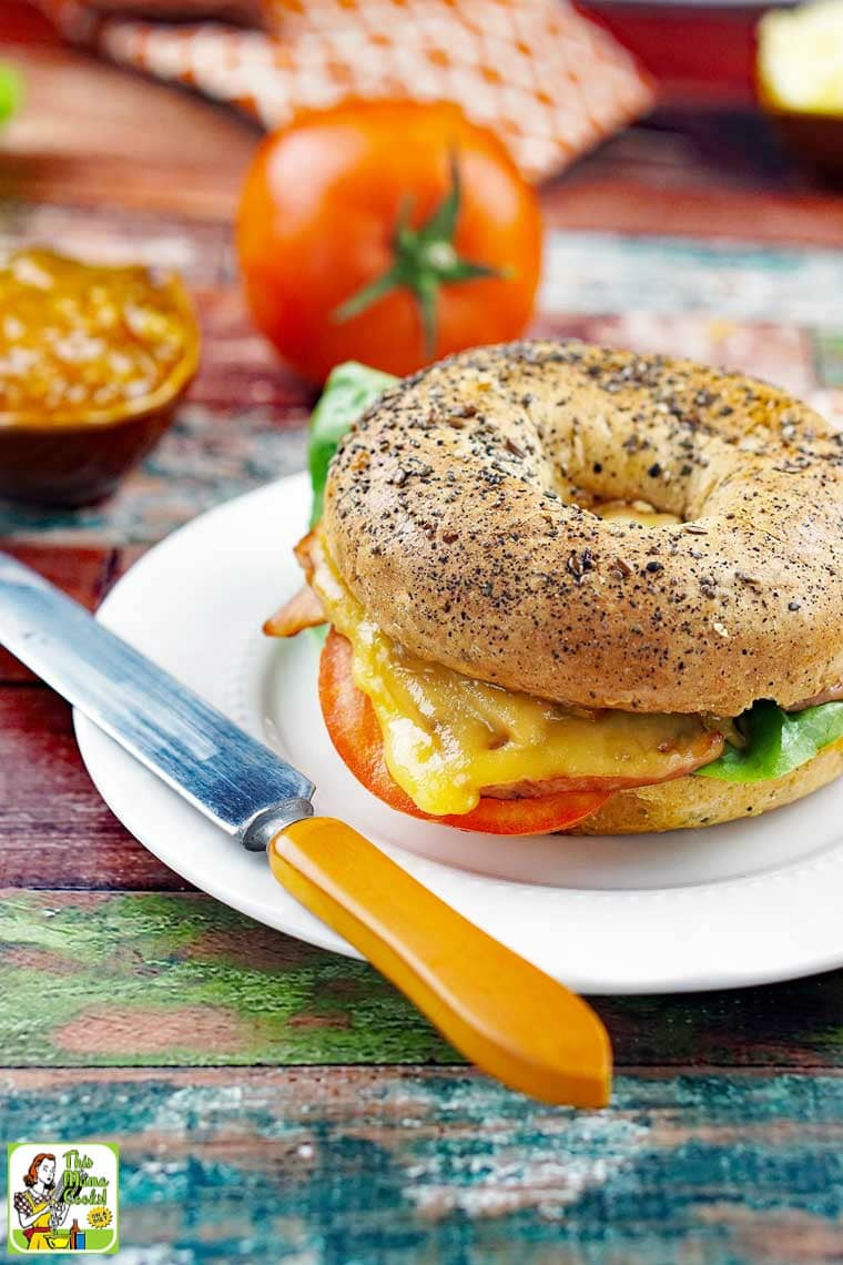 A ham and cheese bagel sandwich on a white plate with a knife.