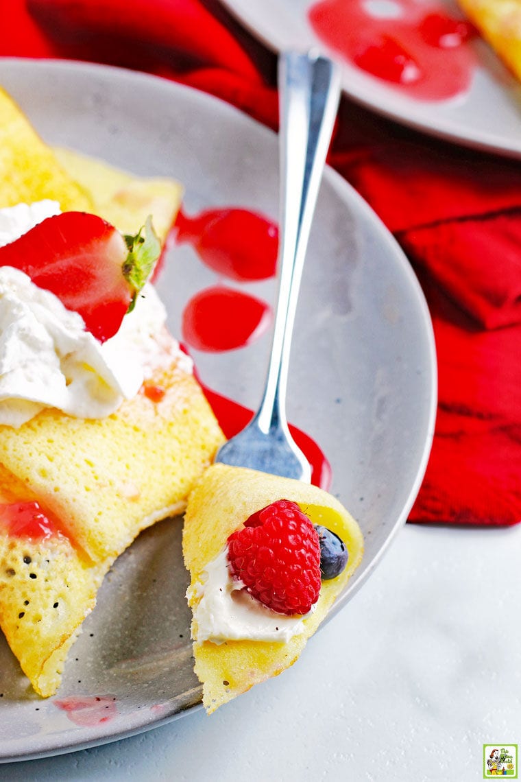 A plate and forkful of gluten free crepe with whipped cream and strawberry sauce.