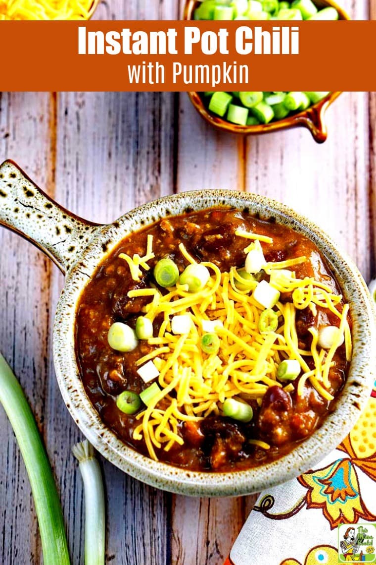 Overhead view of a close up of Instant Pot Chili with Pumpkin with shredded cheese and chopped green onions served in a lug handled bowl.