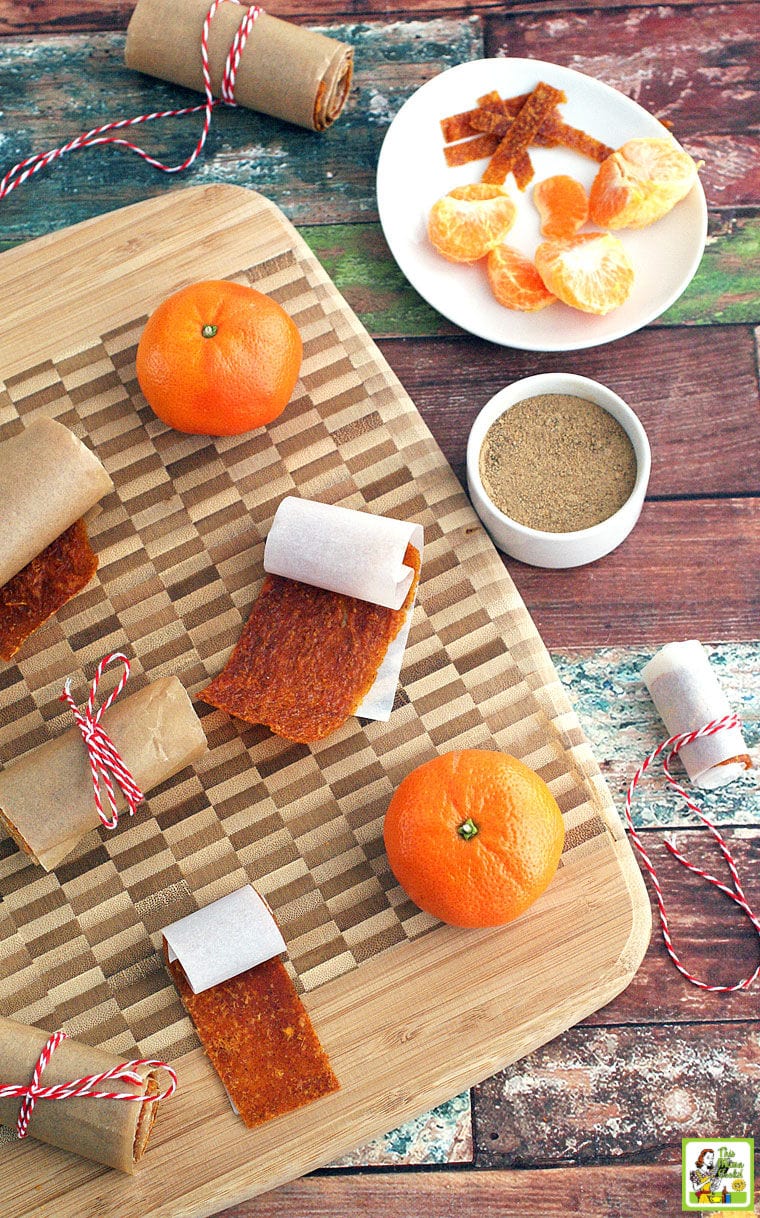 Orange Fruit Leather rollups, oranges, and spices on a wooden cutting board.