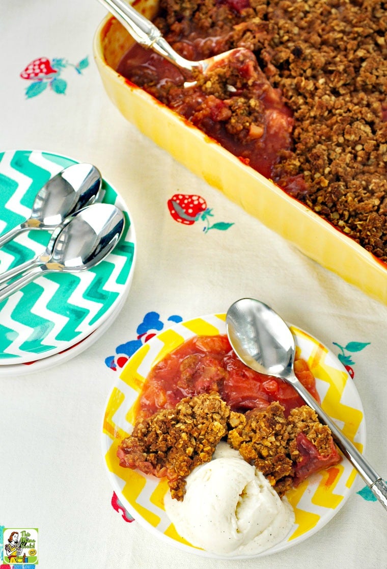 Overhead view of a small  plate of rhubarb crisp and a casserole dish rhubarb crisp with more plates and spoons.