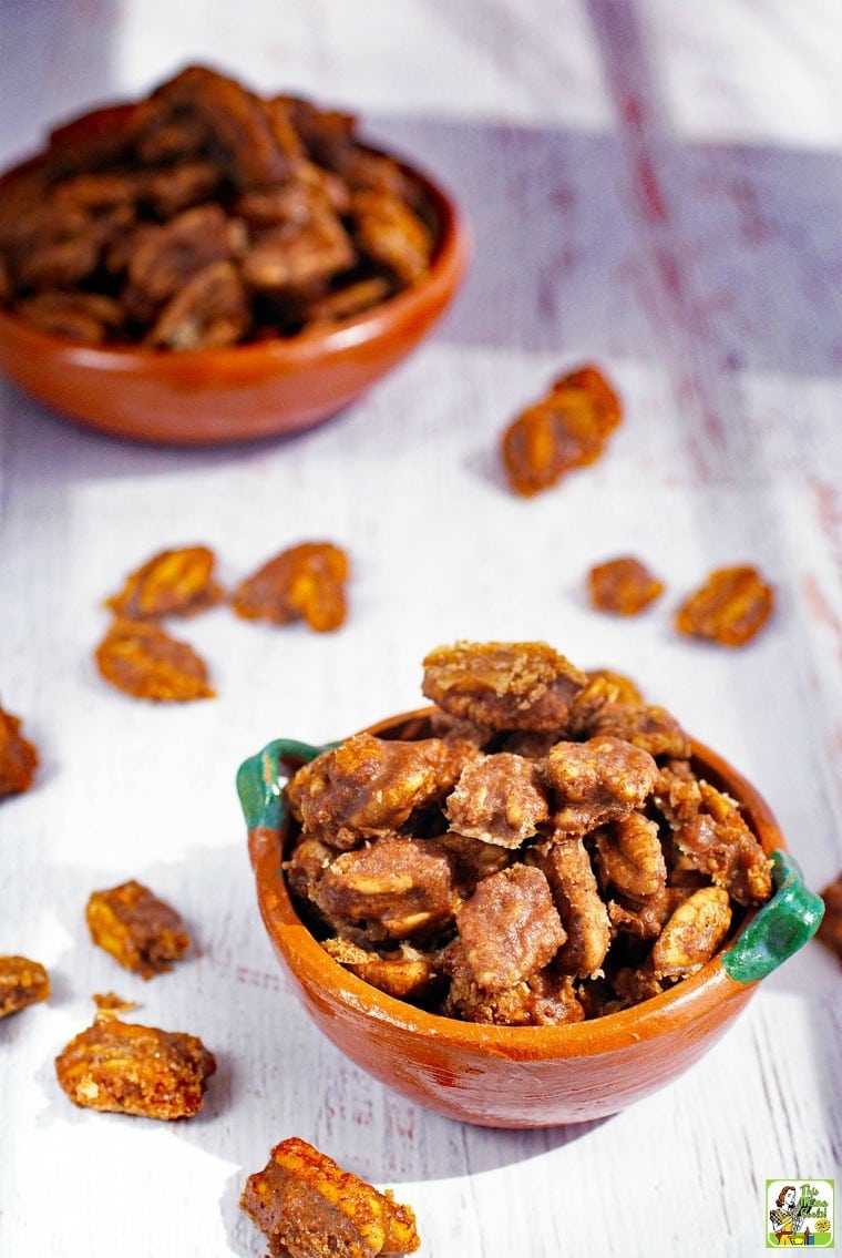 Bowls of Candied Pecans with pecans spread over the tabletop.