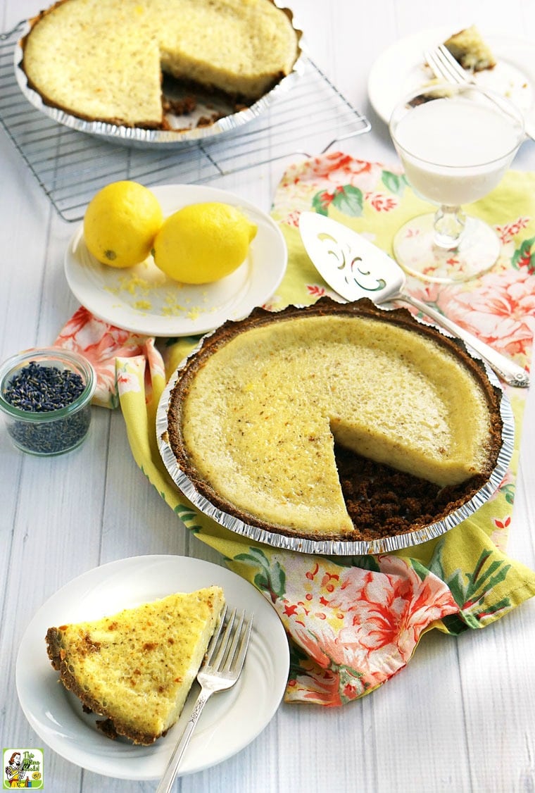 A slice of old fashioned buttermilk pie on a white plate with fork with lemon and lavender.