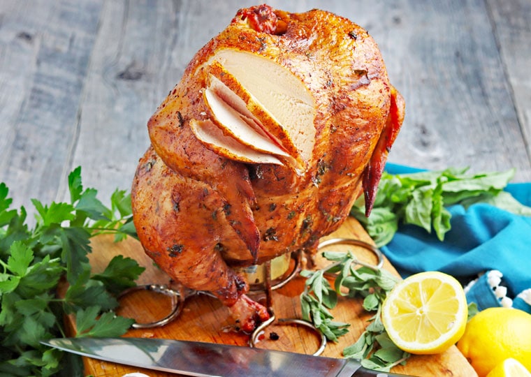 Sliced smoked beer can chicken on a cutting board with a knife and lemons.