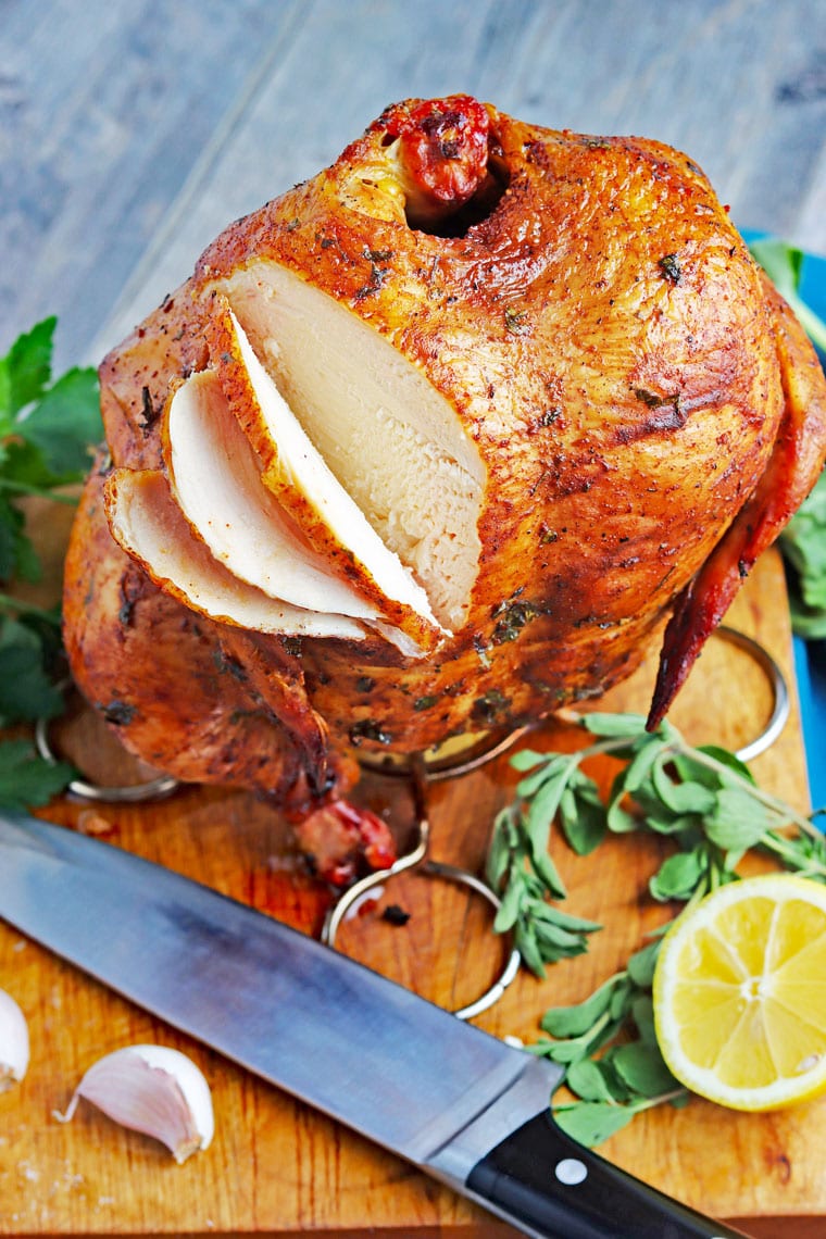  Lata de cerveza ahumada en rodajas de pollo en una tabla de cortar de madera con un cuchillo, limón y hierbas frescas.