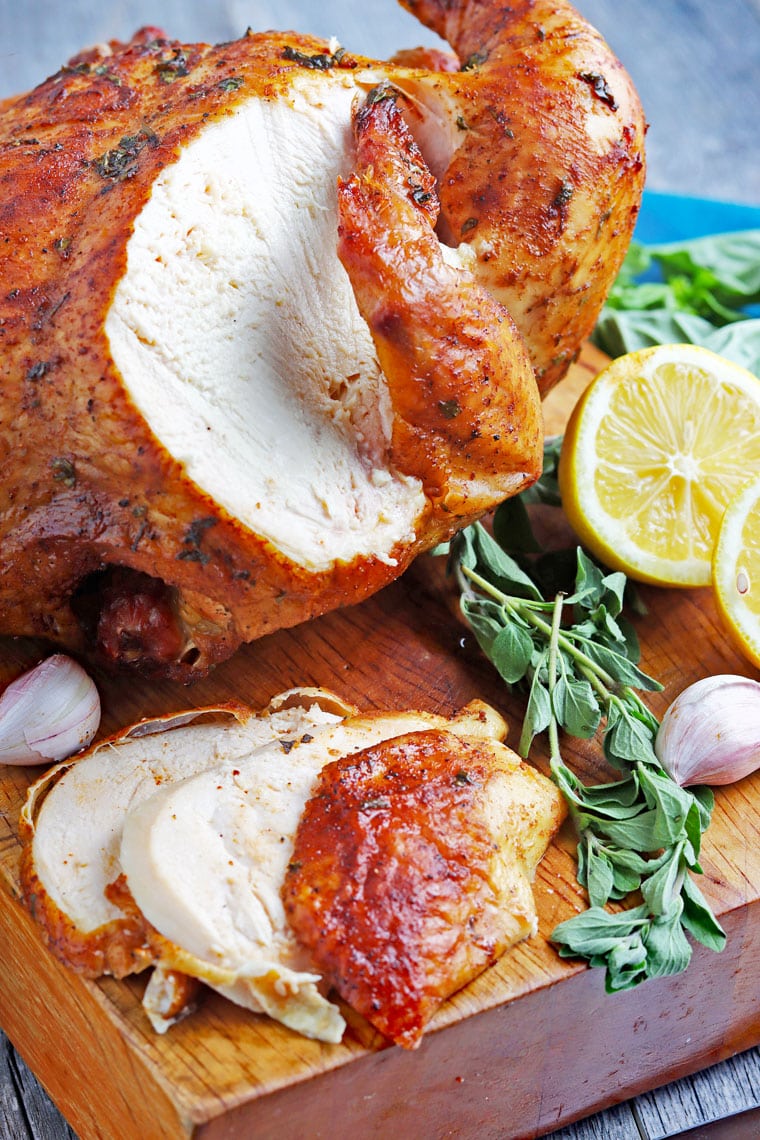  Poulet rôti en tranches avec des morceaux de poulet sur une planche à découper en bois avec des herbes et du citron et de l'ail tranchés.