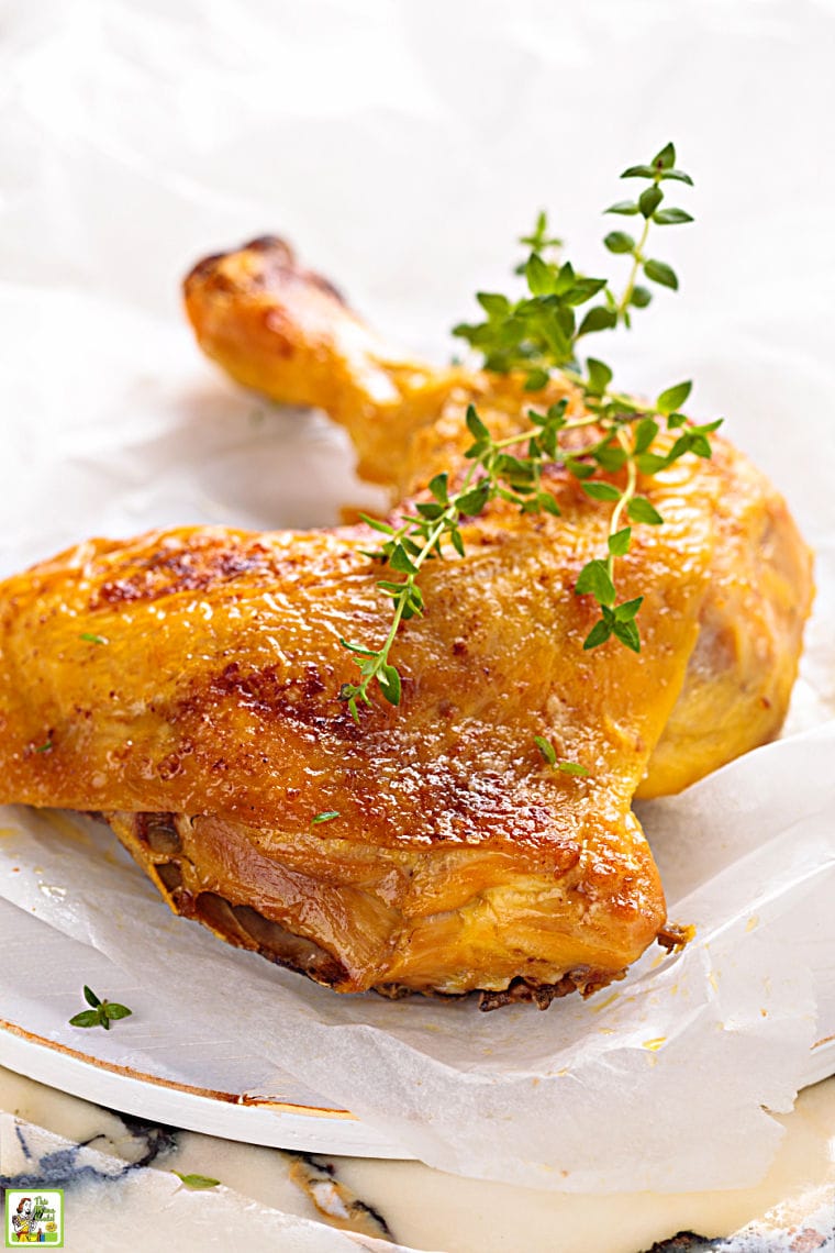 Smoked chicken leg quarters with a sprig of thyme on a white plate.