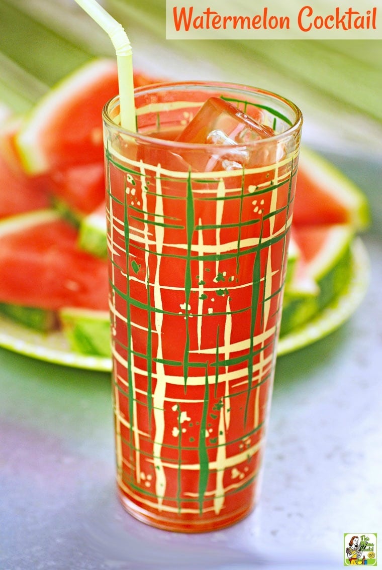 A watermelon cocktail in a tall glass on a metal tray with slices of watermelon.