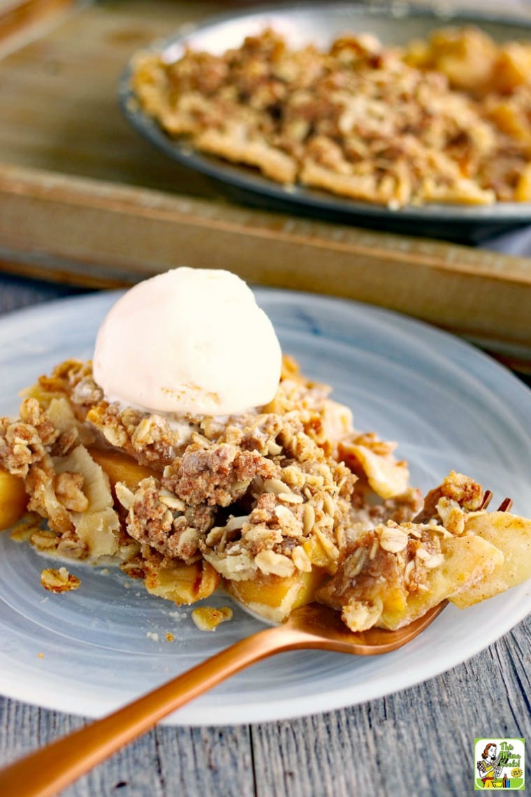 Closeup of a slice of peach and apple pie with a scoop of vanilla ice cream on a glass plate with a copper fork.