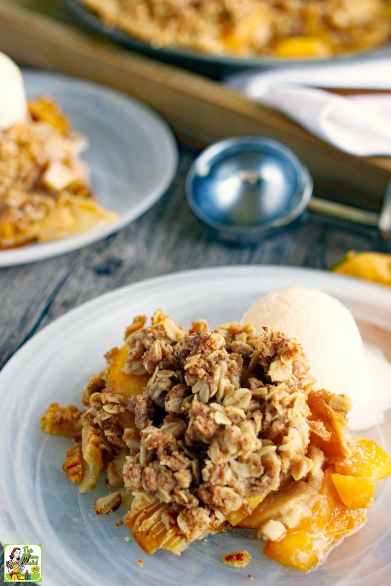 Peach pie with crumble topping with a scoop of vanilla ice cream on a glass plate with an ice cream scooper.