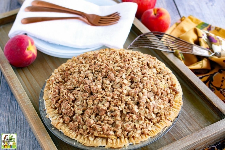 A gluten free apple peach with crumb crust on a wooden tray with plates, napkins, forks, and pie server.